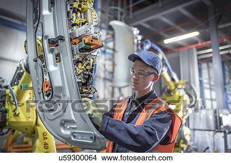 Picture - Apprentice engineer adjusting robot in car factory. Fotosearch