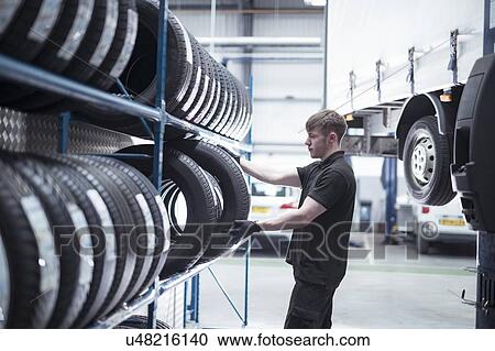 Stock Image - Apprentice engineer selecting tyres in car service centre. Fotosearch