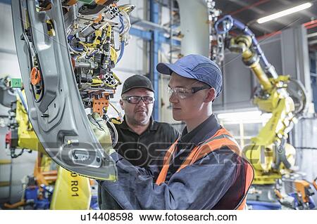 Stock Photo - Apprentice engineer with mentor and robots in car factory. Fotosearch