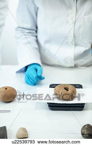 Stock Image - Archaeologist measuring prehistoric weight on a scale. Fotosearch