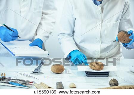 Stock Photo - Archaeologist measuring prehistoric weight on a scale. Fotosearch