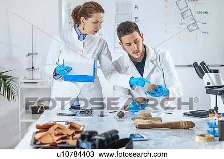 Stock Image - Archaeologists analyzing ancient weight in laboratory. Fotosearch