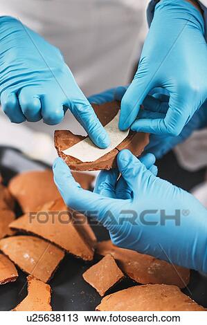 Stock Image - Archaeologists reconstructing broken pottery. Fotosearch
