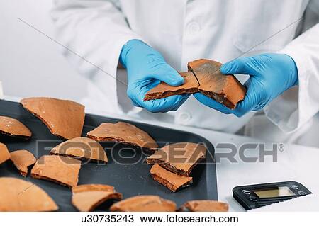 Stock Image - Archaeologists reconstructing broken pottery. Fotosearch