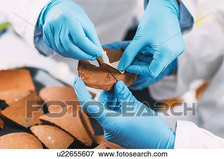 Stock Photo - Archaeologists reconstructing broken pottery. Fotosearch