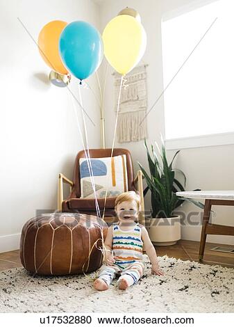 Baby boy holding balloons in living room View Large Photo Image Stock Image - Baby boy holding balloons in living room. Fotosearch