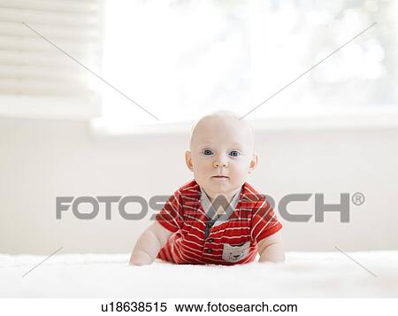 Stock Photography - Baby boy wearing striped romper on bed. Fotosearch