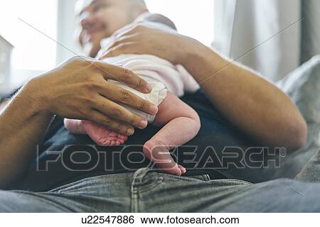 Stock Photograph - Baby resting on father's chest at home. Fotosearch