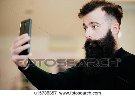Stock Photo - Bearded man taking selfie in barber shop. Fotosearch