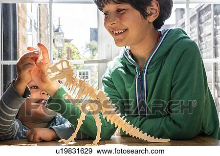 Stock Photo - Boy and little brother playing with wooden dinosaur. Fotosearch