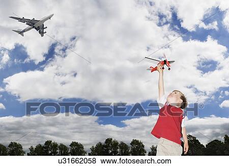 Boy playing with toy plane with plane flying overhead View Large Photo Image Stock Photo - Boy playing with toy plane with plane flying overhead. Fotosearch