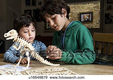 Stock Photo - Boy showing brother way to build wooden dinosaur. Fotosearch