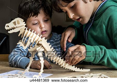 Stock Photo - Boy showing brother way to build wooden dinosaur. Fotosearch