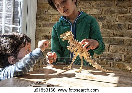 Stock Photo - Boy showing brother way to build wooden dinosaur. Fotosearch