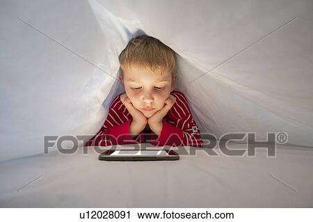Stock Image - Boy using smartphone under bed covers. Fotosearch