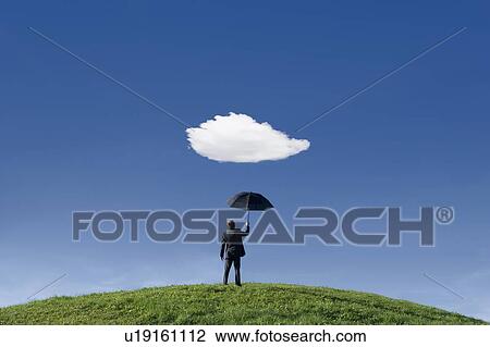 Stock Image - Businessman holding umbrella underneath a single cloud. Fotosearch