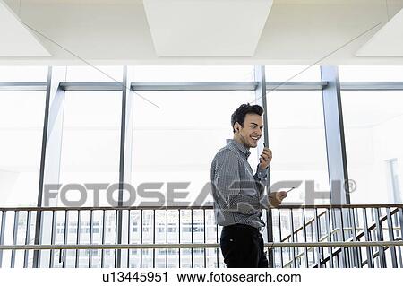 Stock Image - Businessman using smartphone in office corridor. Fotosearch