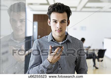 Stock Image - Businessman using smartphone in office corridor, colleague reading in background. Fotosearch