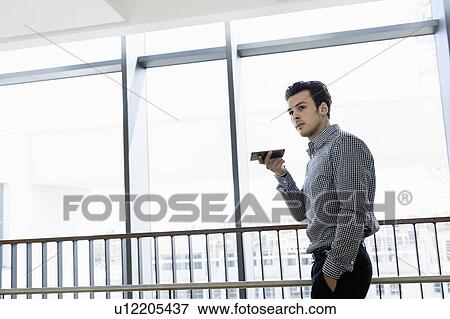 Stock Photo - Businessman using smartphone in office corridor. Fotosearch