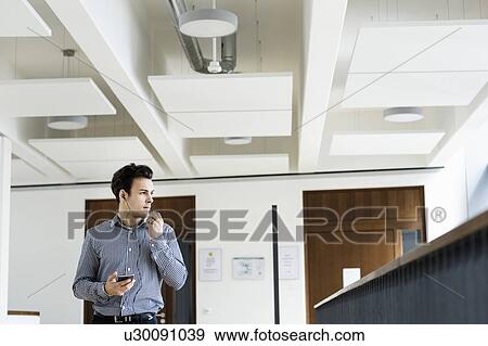 Businessman using smartphone in office corridor View Large Photo Image Stock Photo - Businessman using smartphone in office corridor. Fotosearch