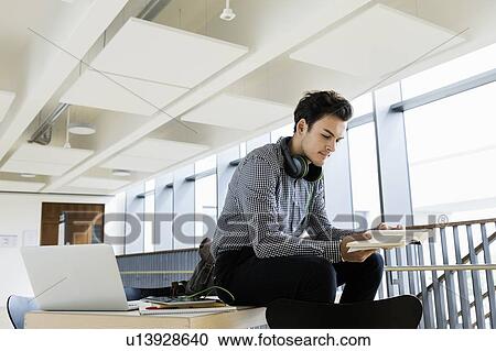 Stock Image - Businessman with headphones reading book in office. Fotosearch