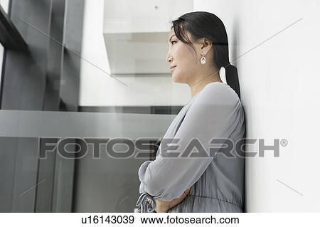 Stock Photo - Businesswoman leaning against white wall in office. Fotosearch