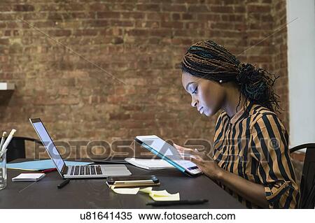 Stock Photography - Businesswoman using digital tablet, laptop and cellphone on desk. Fotosearch