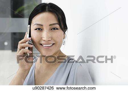 Stock Photograph - Businesswoman using smartphone against white wall in office. Fotosearch