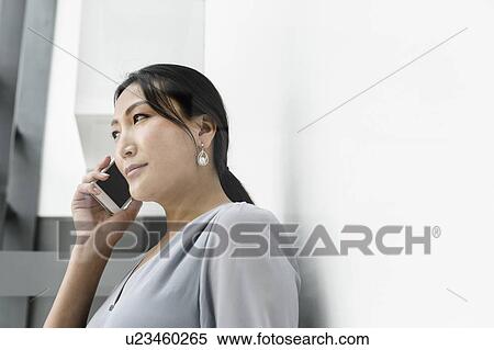 Stock Photography - Businesswoman using smartphone against white wall in office. Fotosearch