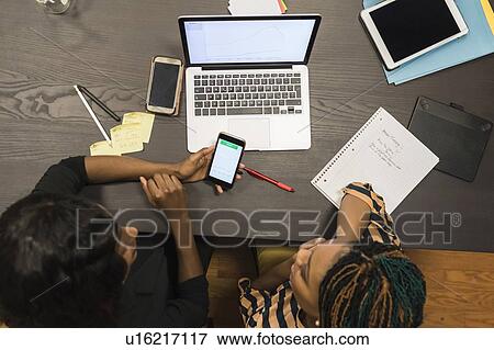 Stock Photo - Businesswomen analysing work using laptop and cellphone. Fotosearch