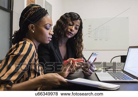 Stock Photo - Businesswomen analysing work using laptop and cellphone. Fotosearch