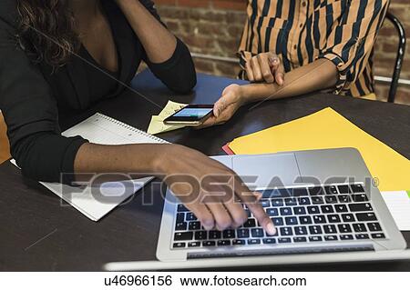 Businesswomen analysing work using laptop and cellphone View Large Photo Image Stock Photograph - Businesswomen analysing work using laptop and cellphone. Fotosearch