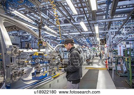 Stock Image - Car worker fitting parts on production line in car factory. Fotosearch
