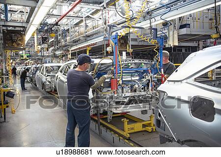 Stock Image - Car workers fitting bonnets to cars on production line in car factory. Fotosearch