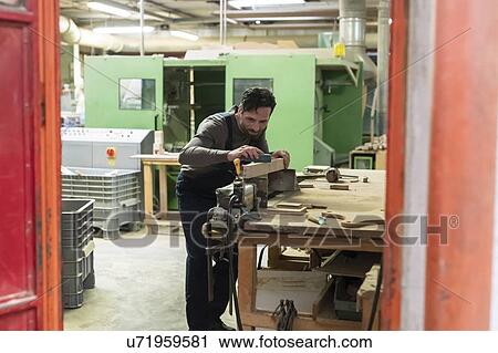 Stock Image - Carpenter sanding wooden furniture leg in factory. Fotosearch