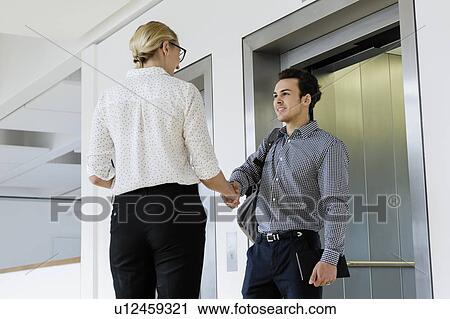 Colleagues shaking hands and talking near elevator View Large Photo Image Stock Image - Colleagues shaking hands and talking near elevator. Fotosearch