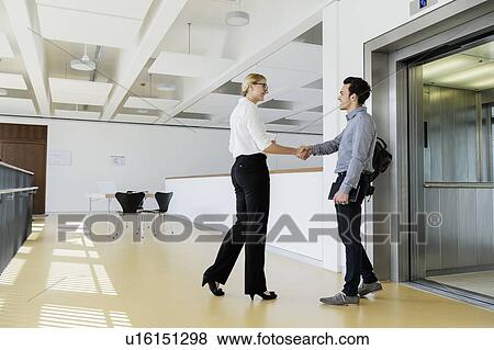 Colleagues shaking hands and talking near elevator View Large Photo Image Stock Photo - Colleagues shaking hands and talking near elevator. Fotosearch