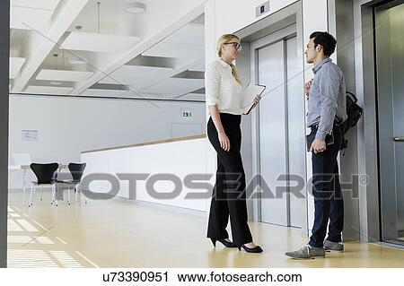 Stock Image - Colleagues talking near elevator. Fotosearch
