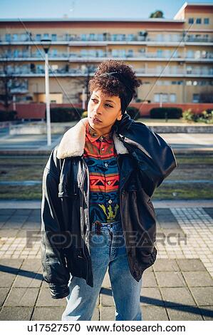 Stock Image - Cool young woman on urban sidewalk looking sideways, portrait. Fotosearch