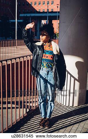 Stock Photography - Cool young woman shielding eyes on sunlit city sidewalk. Fotosearch