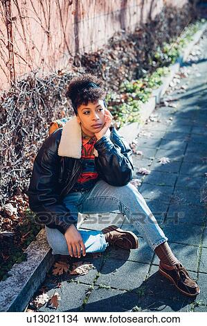 Picture - Cool young woman sitting on urban sidewalk, portrait. Fotosearch