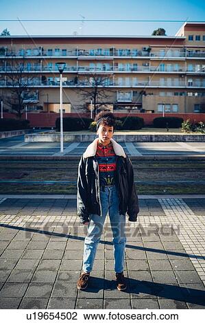 Stock Image - Cool young woman standing on urban sidewalk, portrait. Fotosearch