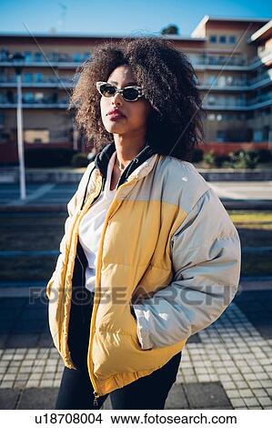 Picture - Cool young woman wearing sunglasses on urban sidewalk, three quarter length portrait. Fotosearch