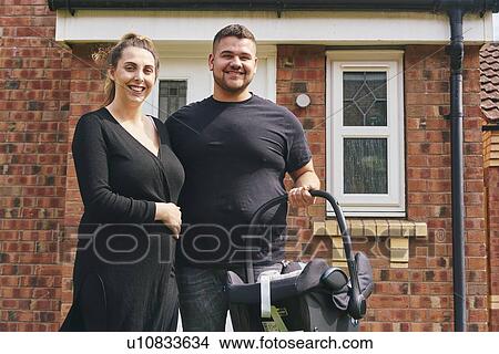 Picture - Couple carrying baby in cradle in front of house. Fotosearch