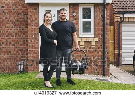 Stock Photo - Couple carrying baby in cradle in front of house. Fotosearch