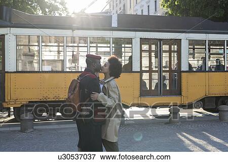 Stock Photo - Couple kissing in street, tram passing in background, Milan, Italy. Fotosearch
