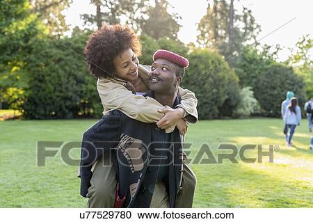 Stock Image - Couple playing piggyback in park, Milan, Italy. Fotosearch