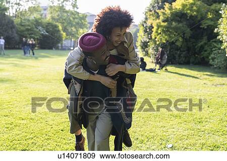 Stock Photo - Couple playing piggyback in park, Milan, Italy. Fotosearch