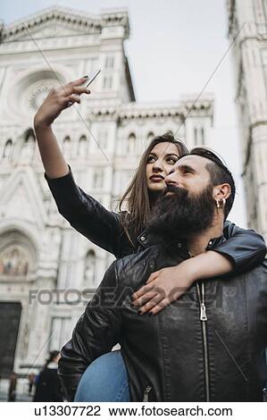 Stock Image - Couple playing piggyback ride and taking selfie, Santa Maria del Fiore, Firenze, Toscana, Italy. Fotosearch