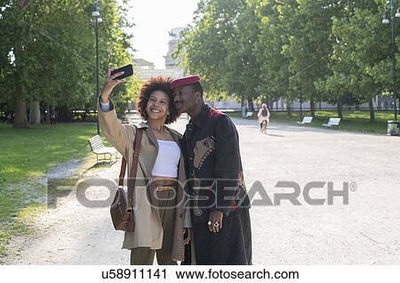Stock Image - Couple taking selfie in park, Milan, Italy. Fotosearch